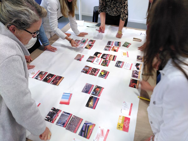 Participants penchés autour d'une grande table recouverte de papier blanc où ils disposent des cartes pour cartographier les impacts d'un événement, lors d'une Fresque de l'Événementiel